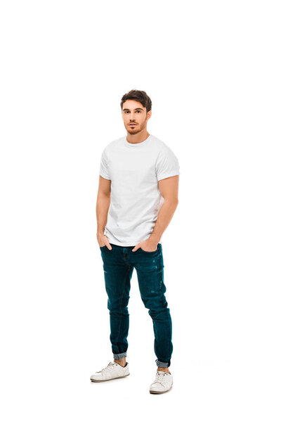 full length view of handsome young man standing with hands in pockets and looking at camera isolated on white