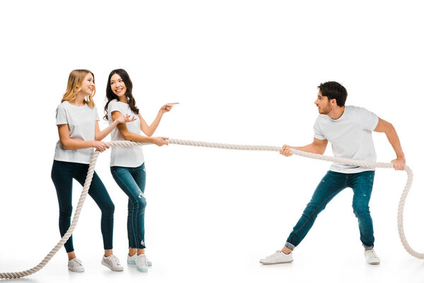 smiling young women and concentrated man pulling rope isolated on white