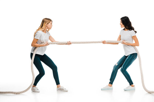 angry young women pulling rope and looking at each other isolated on white