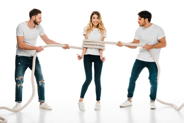 young men holding rope wrapped around smiling young woman showing thumbs up and looking at camera isolated on white