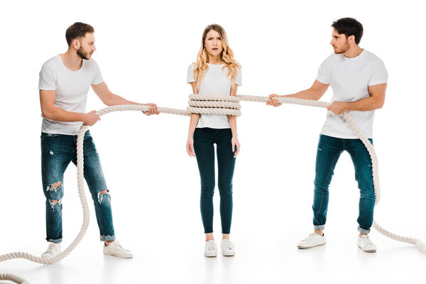young men holding rope wrapped around scared young woman looking at camera isolated on white