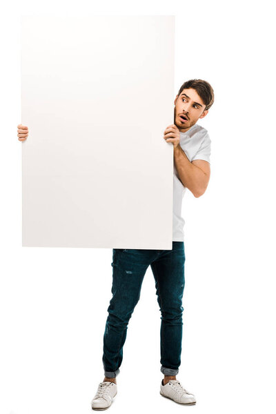 scared young man holding blank banner and looking at copy space isolated on white