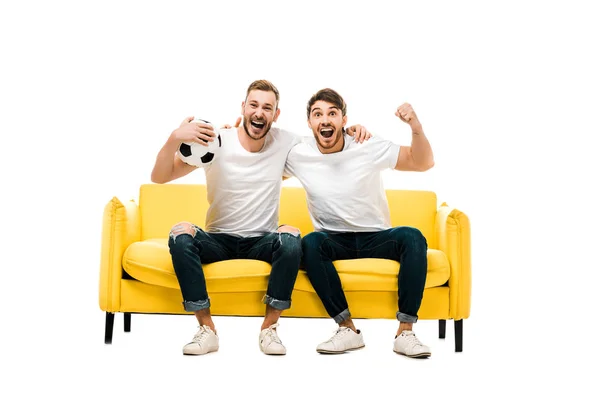 excited young man sitting on couch with soccer ball isolated on white