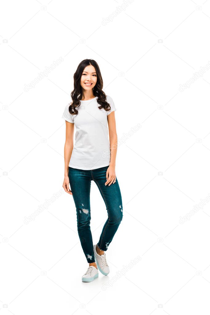 full length view of beautiful brunette girl in white t-shirt and jeans smiling at camera isolated on white