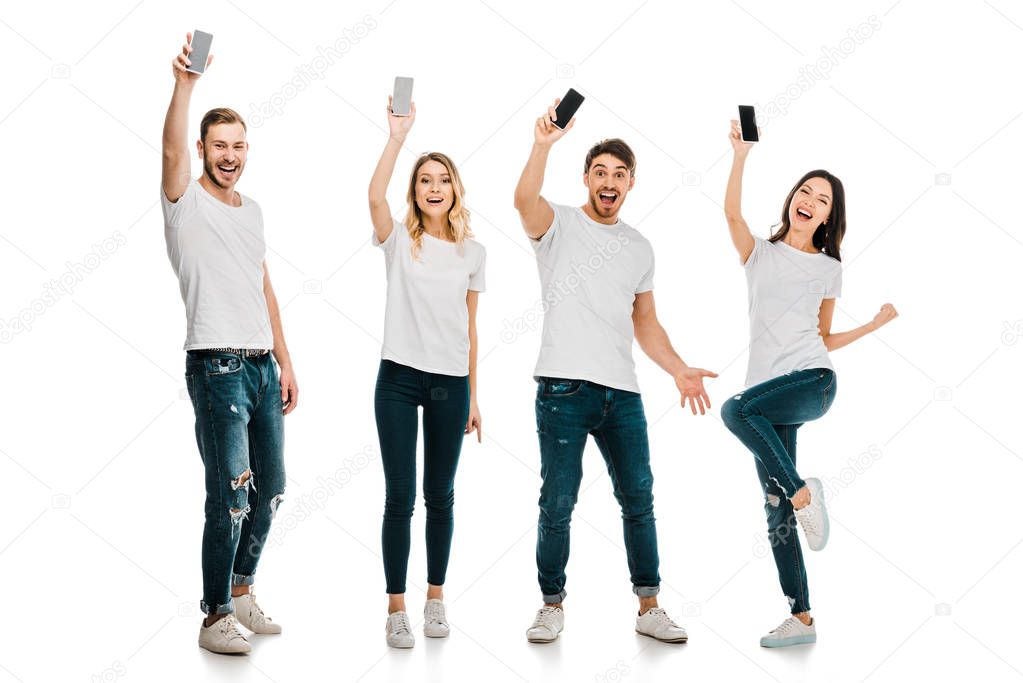 full length view of happy young men and women holding smartphones and smiling at camera isolated on white