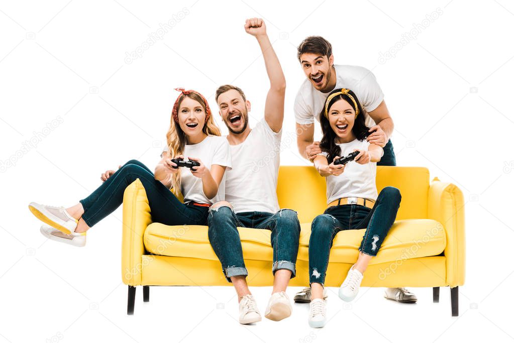 excited young friends playing with joysticks and smiling at camera isolated on white 