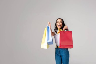 Renkli alışveriş torbaları üzerinde yükseltilmiş el ele tutuşarak ve gri izole kamera bakarak gülümseyen Asyalı kadın