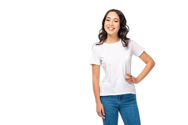 Привлекательная азиатская женщина в белой футболке и синих джинсах держась за руку на бедре изолированы на белом
