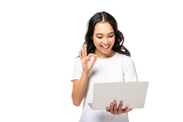 young asian woman using laptop and showing ok gesture isolated on white