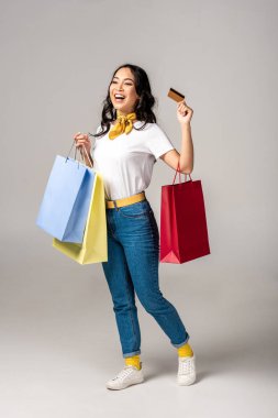 Trendy renkli alışveriş torbaları tutarak ve kredi kartı gri gösteren Asyalı kadın giyinmiş
