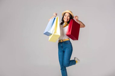 Mutlu trendy renkli alışveriş torbaları gri izole kabarık ellerinde tutan Asyalı kadın giyinmiş