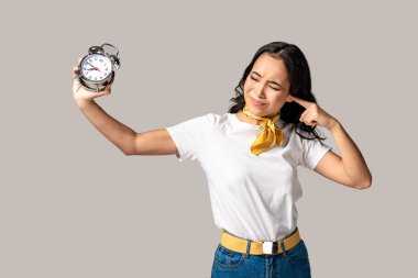Asyalı kadın ile çalar saat uzatılmış elinde tutan ve gri izole işaret parmağı ile kulak kapanış kapalı gözler 