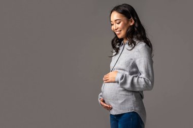 Karın gri izole elle tutan gülümseyen hamile Asyalı kadın