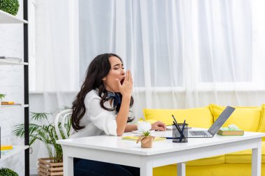 Sleepy asian freelance sitting at work desk and yawing with covering mouth with hand clipart