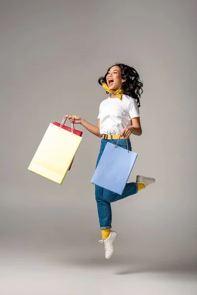 グレーのカラフルなショッピング バッグを持ちながら幸せな笑顔でジャンプ アップの美しい若いアジア女性 — ストック写真