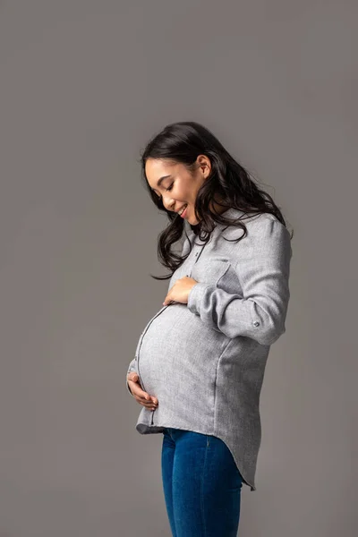 幸せな妊娠中のアジアの女性の腹を見て笑顔に分離グレー — ストック写真