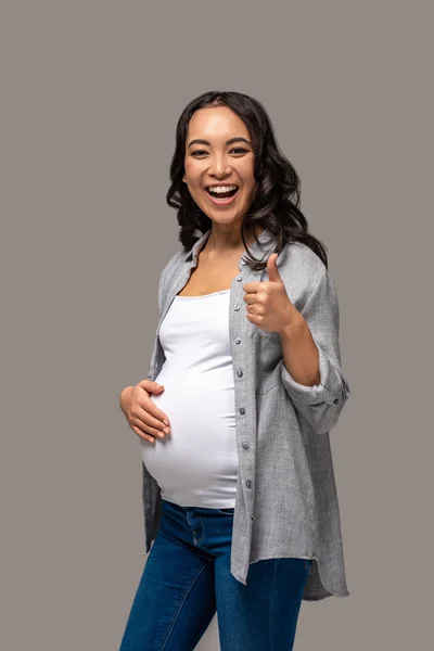 Sorridente Incinta Asiatico Donna Toccare Pancia Mostrando Pollice Isolato Grigio — Foto Stock