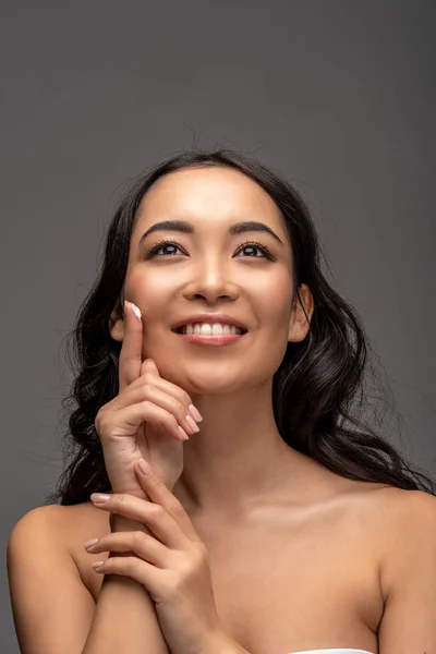 Sorrindo Bela Menina Asiática Aplicando Creme Cosmético Rosto Isolado Cinza — Fotografia de Stock