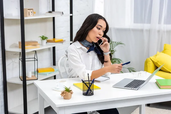 Sério Asiático Freelancer Falando Smartphone Segurando Caneta Enquanto Sentado Casa — Fotografia de Stock