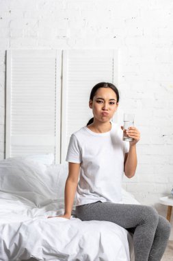 Genç Asyalı kadın beyaz t-shirt sabah yatakta otururken su ile durulama ağız