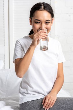 Beyaz t-shirt içme suyu yatakta otururken çekici Asyalı kız