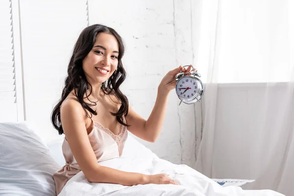 Smiling Beautiful Asian Woman Holding Alarm Clock While Sitting Bed — Stock Photo, Image