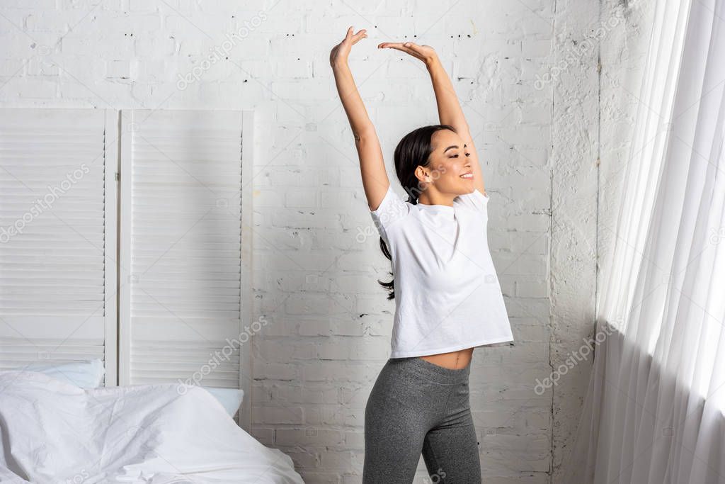 asian woman in white t-shirt and grey leggings doing stretching exercise with raised hands
