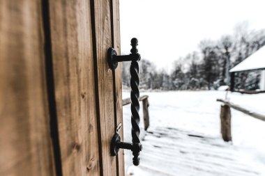 selective focus of opened wooden door with ironshod handle and snowy landscape on background  clipart