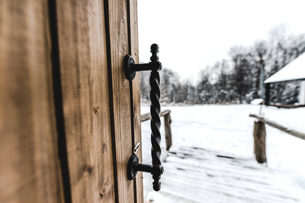 selective focus of opened wooden door with ironshod handle and snowy landscape on background 