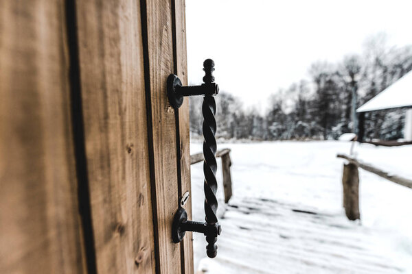 селективный фокус открытой деревянной двери с железной ручкой и снежным ландшафтом на заднем плане
 