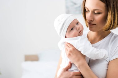 Beyaz tişörtlü genç anne bebeği kucağında tutuyor.