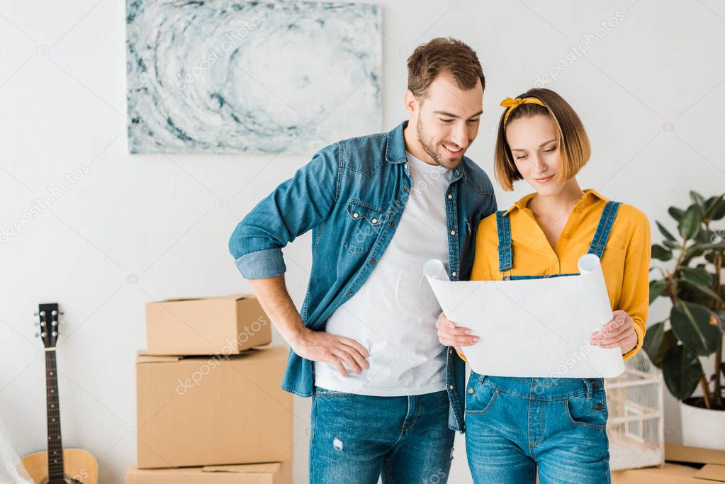 cheerful couple in jeans looking at blueprint at home