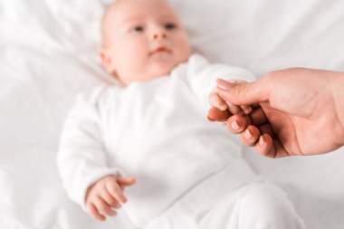 yatakta el ele tutuşan anne ve bebeğin kırpılmış görünümü