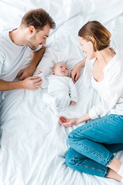 Mutlu ebeveynler beyaz çarşaf üzerinde yatan ve bebek bakarak