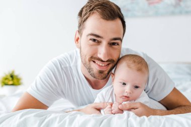 Gülümseyen baba yatak odasında bebek ile yatakta yatıyor