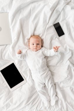 dizüstü bilgisayar, dijital tablet ve boş ekranlı akıllı telefon ile yatakta yatan bebeğin üst görünümü