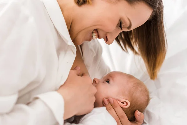 白いTシャツの授乳中の赤ちゃんに微笑む若い母親 — ストック写真