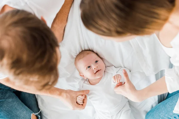 ベッドの上で赤ちゃんと手をつないでいる両親の頭上の眺め — ストック写真