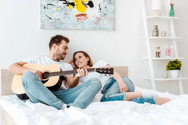 微笑的男人躺在床上和妻子 弹吉他 — 图库照片