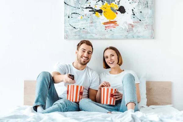 快乐微笑的夫妇在床上吃爆米花和看电视 — 图库照片