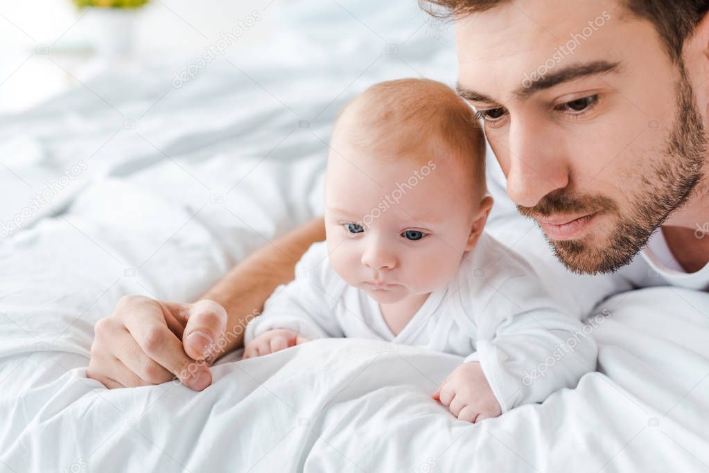 pensive bearded dad with cute baby on bed