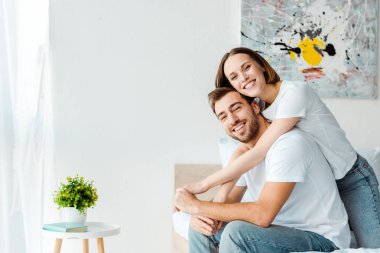 Beyaz t-shirt gülümseyen çift yatak odasında yatakta kucaklayan