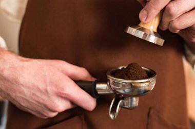 Zemin kahve ve kurcalamak ile portafilter tutan kahverengi önlük barista Kırpılmış görünümü