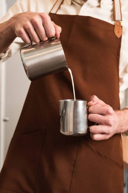 Çelik sürahi süt dökme kahverengi önlük barista kırpılmış görünümü
