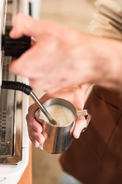 Cropped view of barista filling up steel milk jug clipart