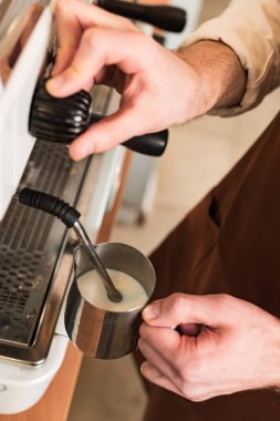 Cropped view of barista filling up steel milk jug clipart