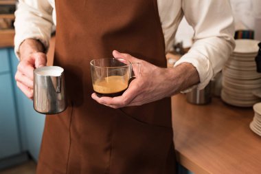 Barista kahve ve süt sürahi fincan tutan kısmi görünümü