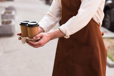 Kahve ile take-out fincan taşıyıcı tutan kahverengi önlük barista kırpılmış görünümü