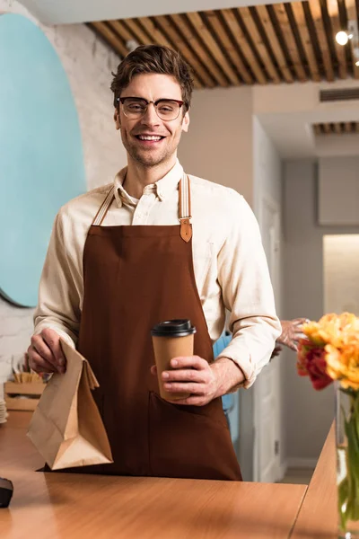 Smiling Barista Glasses Holding Paper Bag Disposable Cup Coffee — Stock Photo, Image