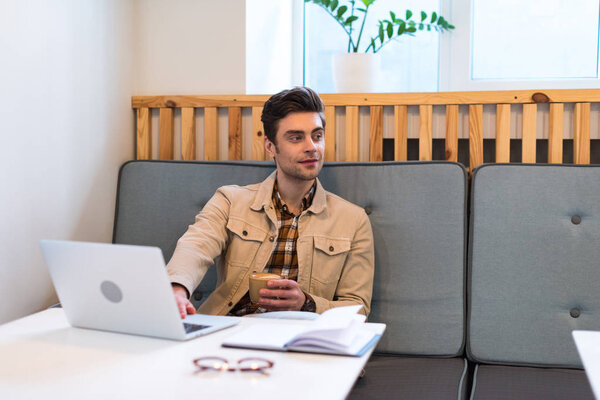 Freelancer with laptop holding cup of coffee in cafe